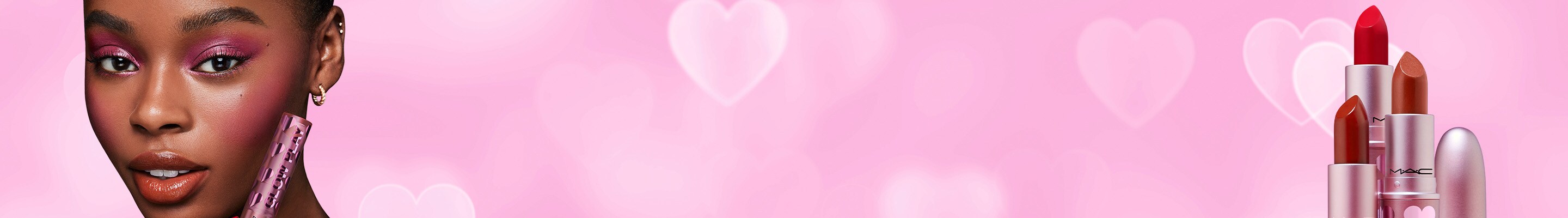 Model and stack of lipsticks on a pink, heart background